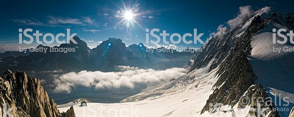 Deep blue high altitude skies and bright sunlight flaring over the jagged spires and rocky ridges, white glaciers and mountain summits of the European Alps in this sweeping panoramic vista. ProPhoto RGB profile for maximum color fidelity and gamut.