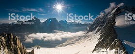 Deep blue high altitude skies and bright sunlight flaring over the jagged spires and rocky ridges, white glaciers and mountain summits of the European Alps in this sweeping panoramic vista. ProPhoto RGB profile for maximum color fidelity and gamut.