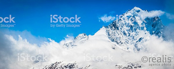 The snow capped summit and dramatic hanging glaciers of the Aiguille Verte (4122m) overlooking the Col des Montets and the swirling clouds below under panoramic deep blue skies, Mont Blanc Massif, France. ProPhoto RGB profile for maximum color fidelity and gamut.