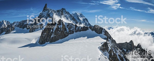 High altitude panoramic view above the clouds across the bright white glaciers, dramatic rocky pinnacles and high altitude summits of the Mont Blanc Massif and the Vallee Blanche from the Pointe Helbronner in Italy past the iconic Alpine peaks of the Aiguille du Midi to the Aiguille Verte and Les Drus, and down the Glacier du Geant down to the Chamonix valley in France. ProPhoto RGB profile for maximum color fidelity and gamut.