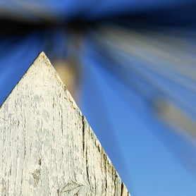 Die Spitze eines Zaunpfahls vor blauem, formenreichem,unscharfem Hintergrund