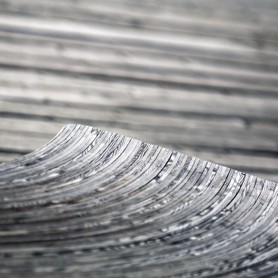 Landscape - Das Ende einer Sitzbank aus Holz mit feiner Musterung setzt sich vor einem Hintergrund mit querlaufender Struktur ab