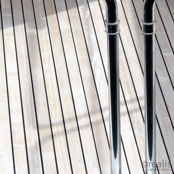 Pride - Zwei edle Stangen aus Chrom werfen einen Schatten auf den edlen Holzboden einer edlen Yacht