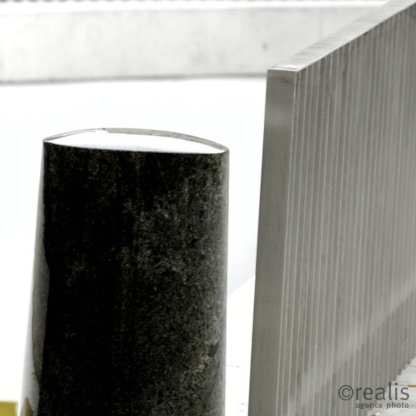 Stamp - Ein schwarzer Pfeiler an einem grauen Zaun schafft eine grafische, abstrakte Wirkung