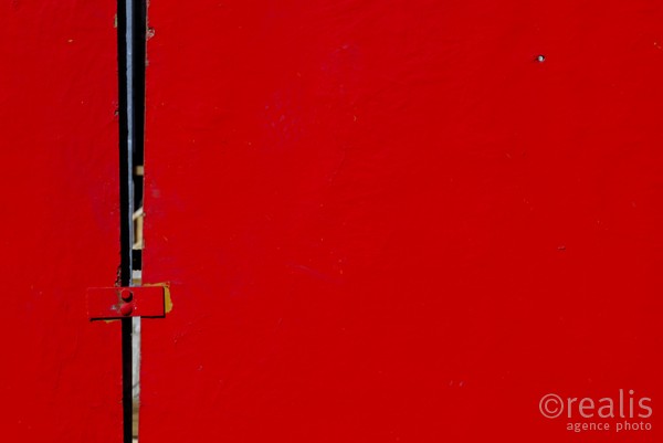 Tension - Zwei rote Bauzäune werden durch ein Eisen zusammengehalten. Eine spaltbreite Öffnung bleibt sichtbar