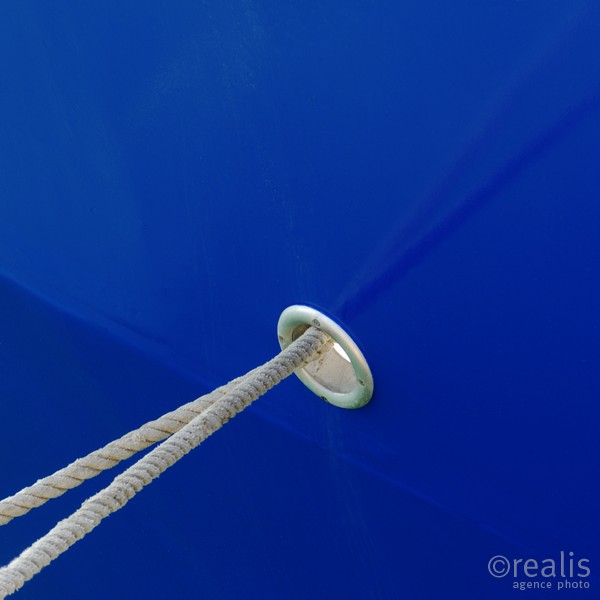The other world - Die Befestigungstaue eines Bootes verlaufen durch eine Öffnung in einer blauen Schiffswand und spiegeln sich an ihr