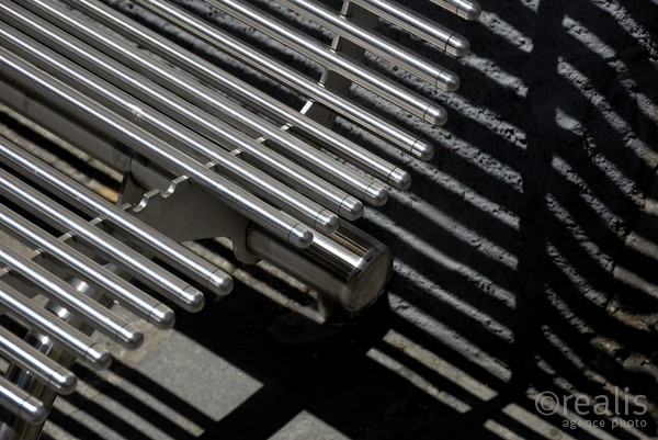 Ze--bra - Der Schatten einer Sitzbank mit Metallstäben wird an einer Wand abgebildet und erzeugt ein Muster von parallelen Geraden