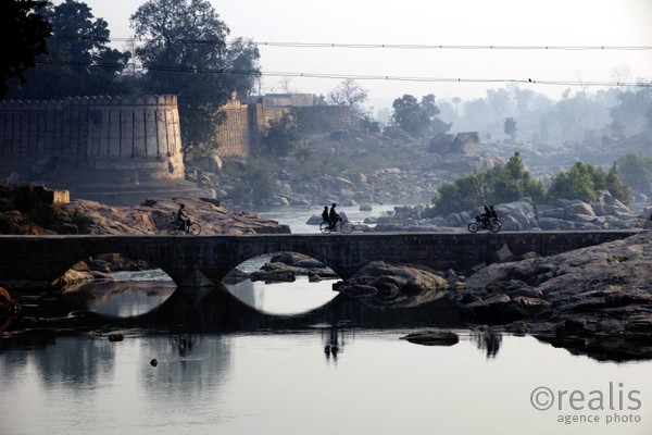 India Follows Raabe 10 - Im Morgengrauen wird eine Brücke über den Ganges von Menschen und Menschen auf Fahrrädern überquert. Die Landschaft spiegelt sich im Fluß.