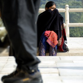 India Follows Raabe 20 - Eine indische Frau versteckt mit ihrem Schleier ihr Gesicht vor einem vorbeikommenden Mann, dessen Beine im Vordergrund zu sehen sind.