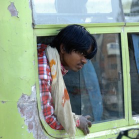 India Follows Raabe 24 - Ein Inder schaut demütig, fragend, neugierig aus dem Fenster eines verlodderten vorbeifahrenden Buses.