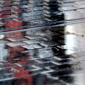 Black meets Red - Ein roter und ein schwarzer Schatten von Menschen spiegeln sich auf dem regennassen Pflaster einer Straße, durch die die Schienen einer Straßenbahn verläuft.