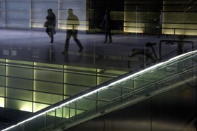 Neon - Drei Menschen schweben in einer Neonwelt durch die Gänge eines Bahnhofs. An einer Rolltreppe lehnt ein abgestelltes Fahrrad. Eine surreale Welt.