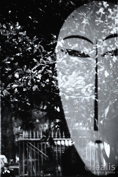 Spring-dawn - Eine abstrahierte Maske spiegelt sich mit den Blättern eines Baumes in einem Fenster und erzeugt so eine geheimnisvolle Stimmung.