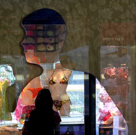 Travel sick - Eine Frau steht vor einem Schaufenster mit ausgestellten Bikinis und dem Schattenbild aus Pappe eines Mannes. Koffer packen und verreisen könnte dem Betrachter in den Sinn kommen