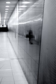 Underground - Das Spiegelbild einer telefonierenden Frau wird in einem U-Bahngang von einem Mann verfolgt, dessen Beine am oberen Bildrand zu sehen sind.