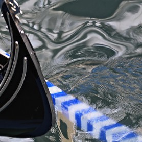 Venice charm - Die schwarze Vorderseite einer venezianischen Gondel spiegelt sich mit dem Vorderteil eines blau-weißen Paddels im Wasser und erzeugt eine sprudelnde, lebendige Gestalt des sie umgebenden Wassers.